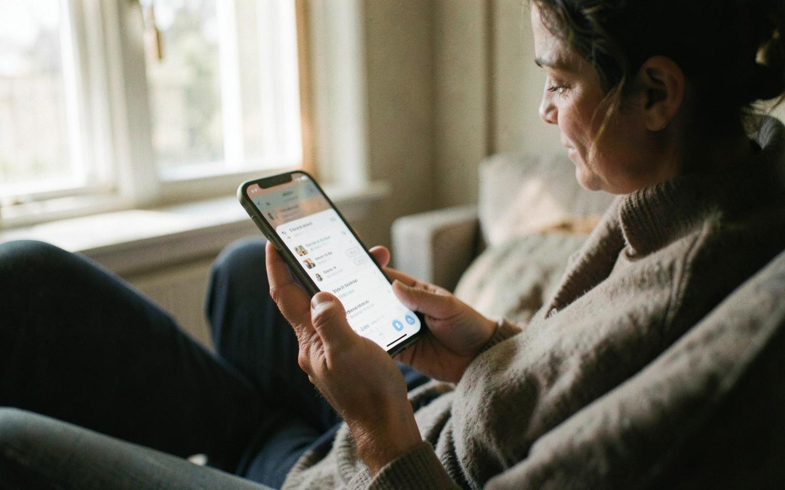 A homeowner on her couch reading search results on her phone while looking for a contractor.